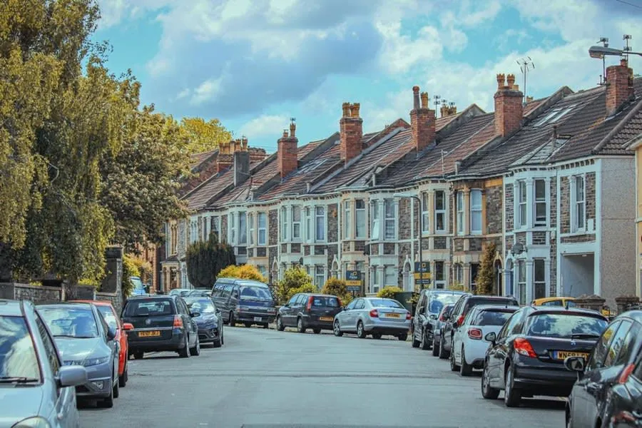 Cars parked nose to tail along a street of traditional English terraced houses