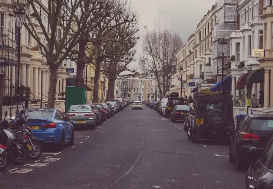 A residential street lined with mature trees and parked cars