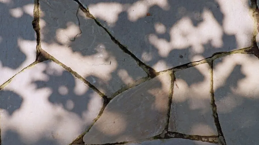 Cracked and uneven stone paving with shadows across the surface